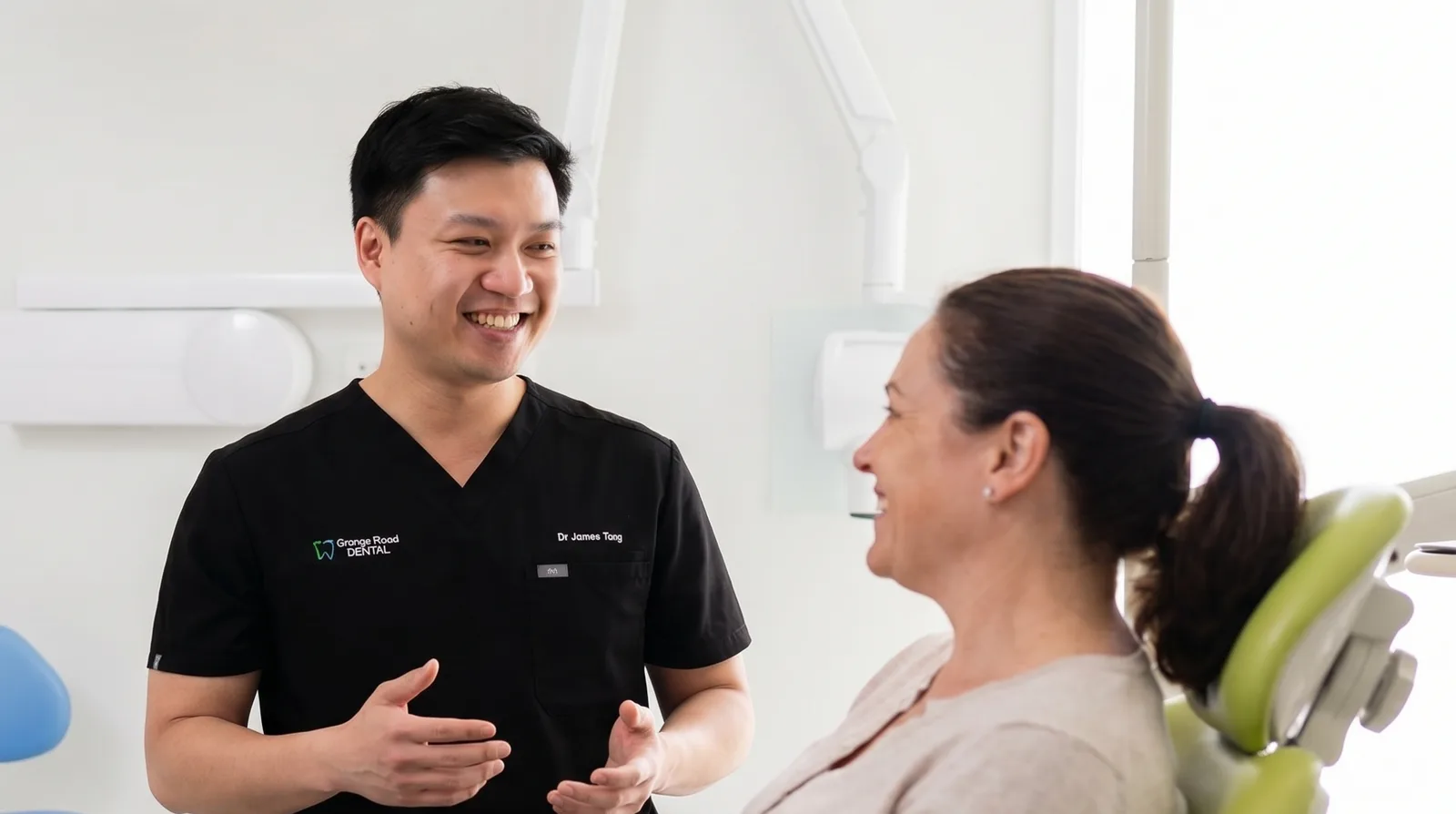 Dr James at Grange Road Dental smiling as he talks a patient through her treatment options while she sits relaxed in the dental chair